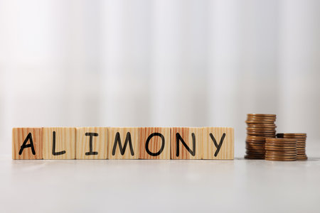 Alimony word made of cubes with letters and stacked coins on tableの写真素材