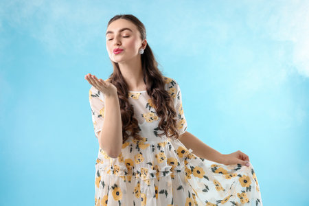 Beautifully dressed young woman blowing kiss on light blue backgroundの写真素材