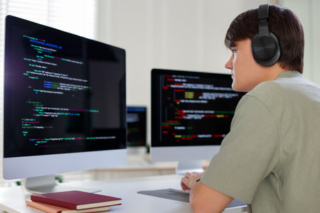 Programmer in headphones working on computer at white table in officeの写真素材