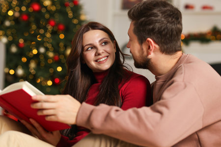 Happy couple reading book together in room decorated for Christmasの写真素材