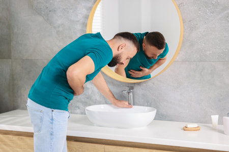 Man suffering from stomach ache and nausea over sink in bathroomの写真素材