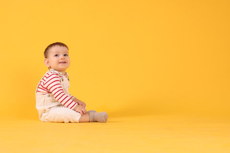 Cute little baby sitting on yellow background, space for textの写真素材