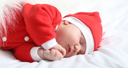 Cute newborn baby in Christmas costume sleeping in bed at homeの写真素材