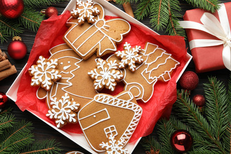 Tasty gingerbread cookies and festive decor on black wooden table, flat lay