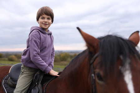 Equine assisted therapy. Little boy riding beautiful horse outdoors. Lovely domesticated petの写真素材