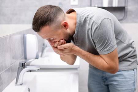 Man suffering from nausea over sink in bathroomの写真素材