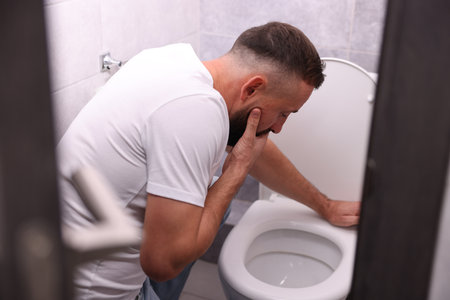 Man suffering from nausea over toilet bowl in bathroomの写真素材