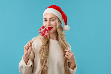 Christmas celebration. Woman in Santa hat with lollipop on light blue backgroundの写真素材