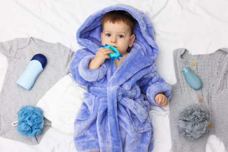 Cute baby in bathrobe, clothes and bathroom accessories on bed, top viewの写真素材