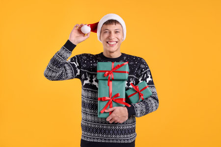 Smiling man in Santa hat with many gift boxes on yellow background. Merry Christmas and Happy holidaysの写真素材