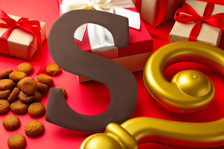 Saint Nicholas (Sinterklaas) day. Crosier, kruidnoten cookies, chocolate letter S and gift boxes on red background, closeupの写真素材