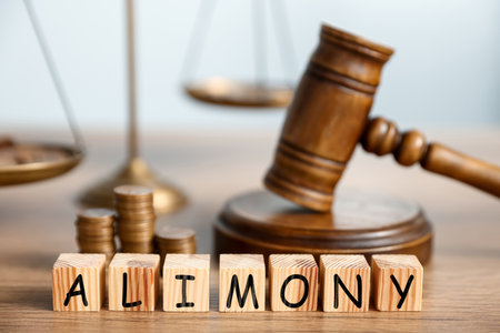 Alimony word made of cubes with letters, judge's gavel, scales of justice and stacked coins on wooden tableの写真素材