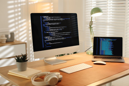 Programmer's workplace with computer, laptop and headphones on wooden table in office