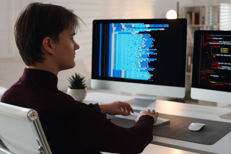 Programmer working on computer with dual monitors at white table in office