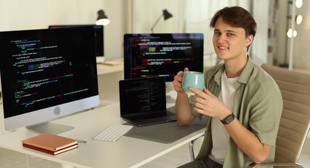 Portrait of smiling programmer with cup on chair at workplace