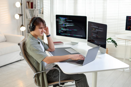 Programmer in headphones working on laptop at white table in officeの写真素材