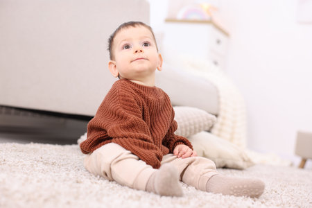 Cute little baby sitting on floor at home, low angle viewの写真素材