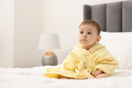 Cute baby in bathrobe on bed at home. Space for textの写真素材