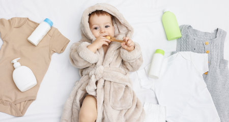 Cute baby in bathrobe, clothes and bathroom accessories on bed, top viewの写真素材