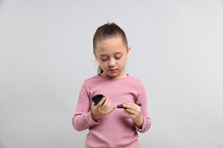 Diabetes. Little girl checking blood sugar level with lancet pen and glucometer on gray backgroundの写真素材