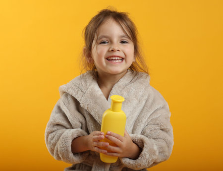 Happy girl in bathrobe with cosmetic product on yellow backgroundの写真素材