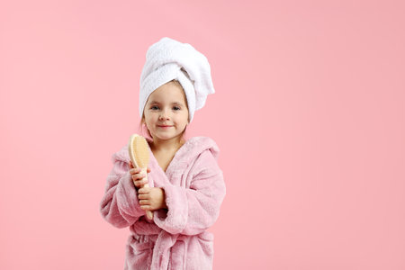 Cute girl in bathrobe with wrapped hair and brush on pink background. Space for textの写真素材