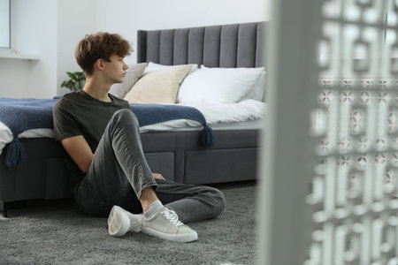 Depressed teenage boy near bed at homeの写真素材