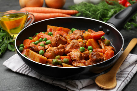 Delicious cooked stew in frying pan and ingredients on black table, closeupの写真素材