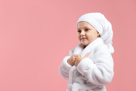 Cute girl in bathrobe with wrapped hair on pink background. Space for textの写真素材