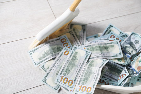Sweeping dollar banknotes with broom into dustpan on light wooden floor, closeupの写真素材
