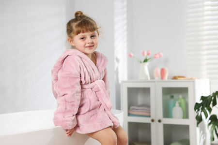 Cute girl in bathrobe near bathtub at home. Space for textの写真素材