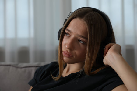 Depressed teenage girl with headphones in armchair at home