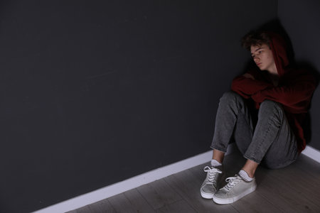 Depressed teenage boy near black wall indoors, space for textの写真素材