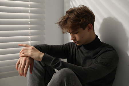 Depressed teenage boy near window at home