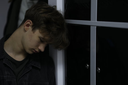Depressed teenage boy near modern lockers indoors
