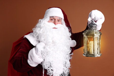Santa Claus with red bag of Christmas gifts and lantern on brown backgroundの写真素材