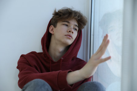 Depressed teenage boy near window at homeの写真素材