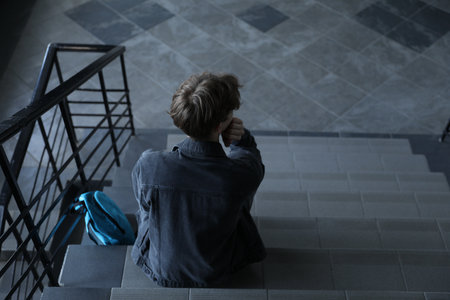 Depressed teenage boy and backpack on stairs indoors, above view. Space for text