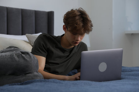 Sad teenage boy with laptop on bed at homeの写真素材