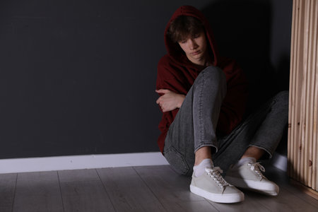Depressed teenage boy near black wall indoors, space for textの写真素材