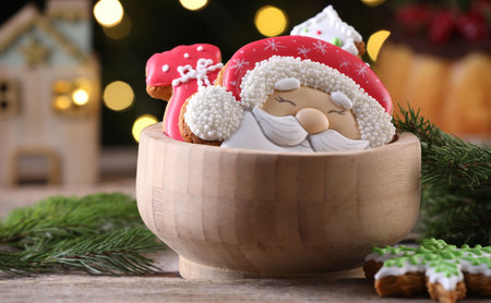 Tasty gingerbread cookies in bowl and fir tree branches on wooden table against blurred lights, closeup. Christmas treatの写真素材