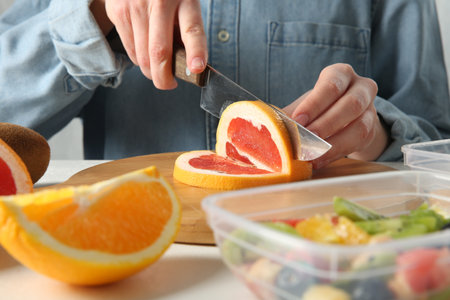 Making fruit salad. Woman cutting grapefruit at white table, closeup