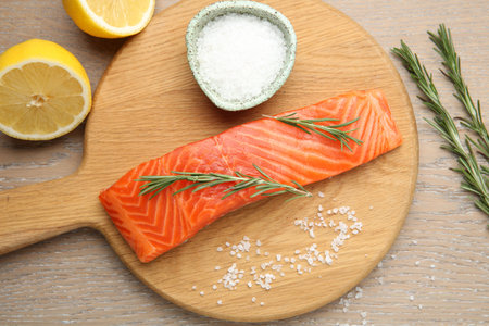 Piece of salmon fillet, rosemary, salt and lemon on wooden table, flat lay