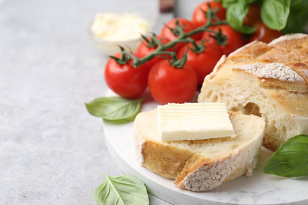 Slices of baguette with butter, basil and tomatoes on light gray table, closeup. Space for textの写真素材