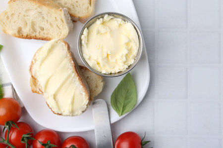 Slices of baguette with butter, basil, tomatoes and knife on white tiled table, flat lay. Space for textの写真素材