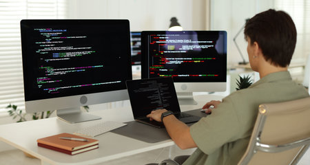 Programmer working on computer and laptop at white table in officeの写真素材