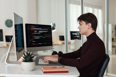 Programmer working on computer with dual monitors at white table in officeの写真素材