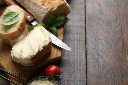 Slices of baguette with butter, basil, tomato and knife on wooden table, closeup. Space for textの写真素材
