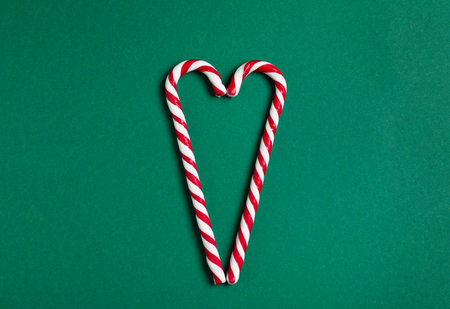 Heart made with candy canes on green background, top view. Christmas treat