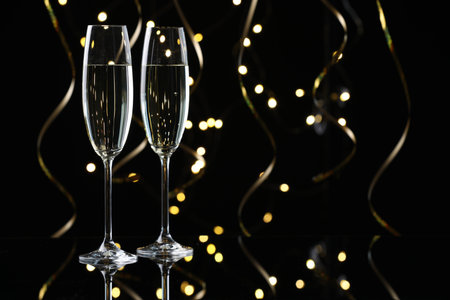 Happy New Year. Sparkling wine in flute glasses and serpentine streamers on black background, bokeh lightsの写真素材
